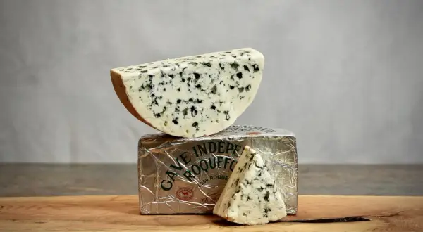 Un morceau de roquefort est posé sur son emballage argenté, avec une autre part en triangle à côté.