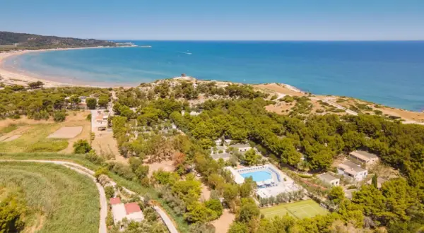 Vista aerea della baia della Tufara con mare azzurro, spiaggia dorata, pineta lussureggiante, piscina e campo da tennis.