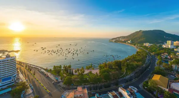 Sonnenuntergang über dem Vung Tau Port mit vielen Booten im Wasser und einer grünen Hügelkette im Hintergrund.
