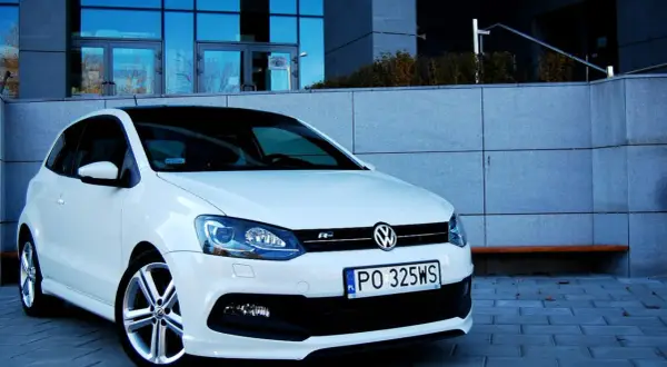 Biały VW Polo 1.2 benzyna z czarnym dachem, zaparkowany przed nowoczesnym budynkiem.