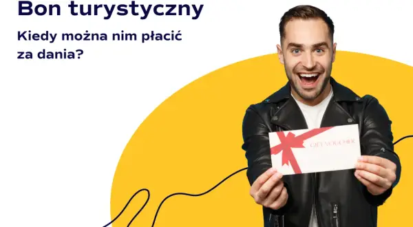 Uśmiechnięty mężczyzna trzyma bon podarunkowy. Czy bon turystyczny można wykorzystać w restauracji na pyszne dania?