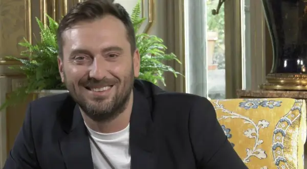 Un uomo sorride, con un blazer scuro e una maglietta bianca. I testi di Cesare Cremonini dicono di me che sono felice.