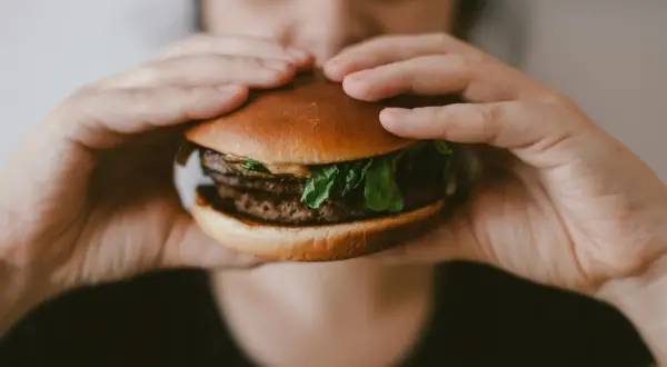 Osoba trzyma rękami soczystego burgera, zastanawiając się, ile kalorii ma burger.