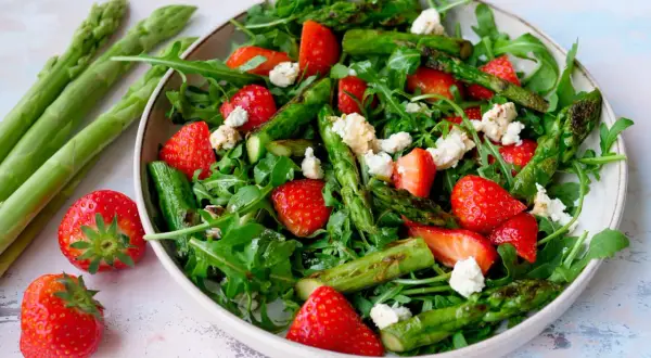 Frischer Spargelsalat mit Erdbeeren und Rucola, garniert mit zerbröseltem Käse.