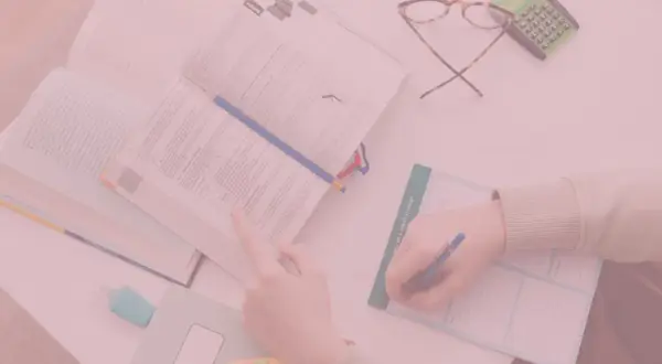 Otwarta książka, ręka pisząca w notatniku, okulary i kalkulator.
