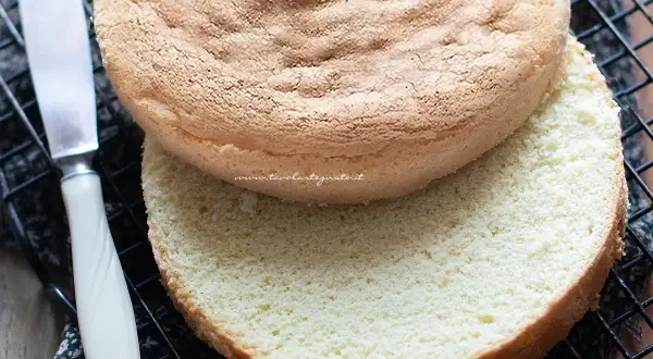 Due dischi di pan di spagna senza glutine, uno sopra l'altro, su una griglia. Un coltello è visibile a sinistra.