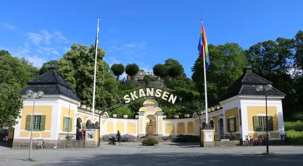 Skansen, Stockholms berömda friluftsmuseum, välkomnar besökare med gula byggnader och en regnbågsflagga.