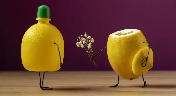 Un limone con gambe di filo offre un mazzolino di fiori a un altro limone con tappo verde. Un divertente shooting still life.