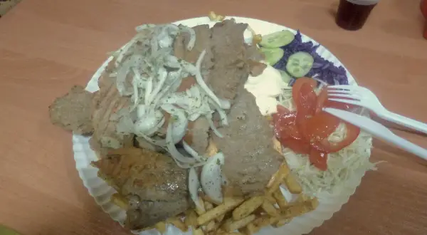 Talerz z kebabem, frytkami, warzywami i napojem.
