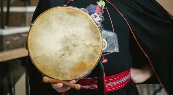 Mateusz Dobrowolski trzyma bębenek. Na czarnej koszulce widnieje wizerunek mężczyzny w kolorowej czapce.