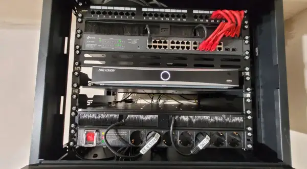 W szafie sieciowej znajduje się router, switch TP-Link, rejestrator Hikvision i listwa zasilająca.