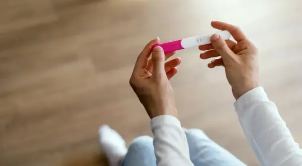 Dłonie trzymające test ciążowy. Wynik wskazuje na wczesny etap, być może 1 tydzień ciąży.