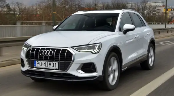 Białe Audi Q3 w ruchu drogowym. Kierowca za kierownicą. Wiele osób szuka audi q3 opinie przed zakupem.