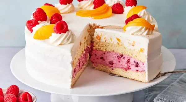 Eine köstliche Pfirsich Melba Torte mit saftigen Himbeeren und Pfirsichstücken, verziert mit Sahnetuffs.