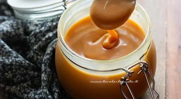 Un cucchiaio raccoglie un denso caramello salato da un barattolo di vetro.