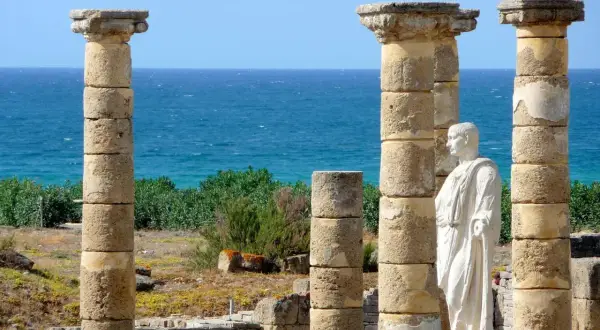 Ruinas romanas en la playa Baelo Claudia, con columnas y una estatua de mármol frente al mar azul.