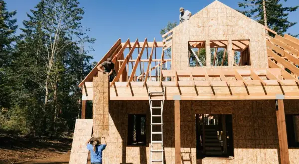 Construcción de una casa de madera, con obreros colocando tableros. El proceso de saber cuanto cuesta hacer una casa es complejo.