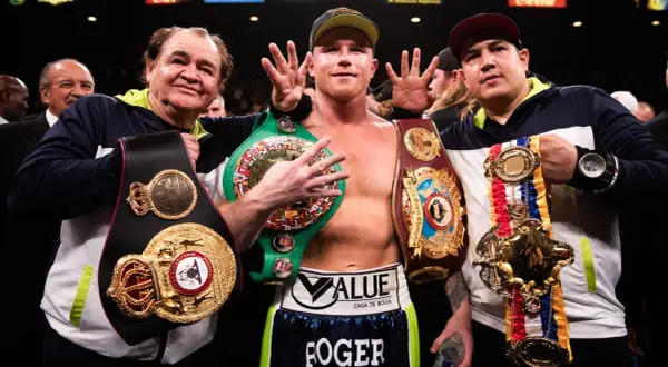 Canelo, flanked by his trainers, proudly displays multiple championship belts, a testament to his incredible win streak.
