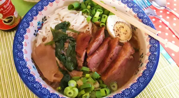 Aromaticzny ramen z kaczki z makaronem ryżowym, jajkiem na twardo, szpinakiem i szczypiorkiem.