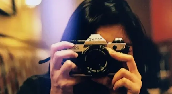 A person holds a Canon AE-1, a classic camera, ready to capture a moment. This camera is the best film for Canon AE-1 enthusiasts.