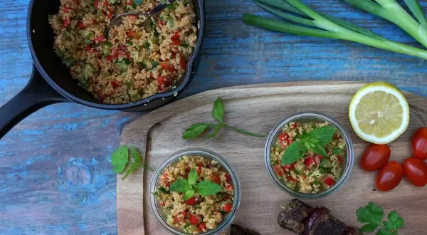Frischer Couscous-Salat mit Tomaten, Gurken und Minze, serviert in Gläsern und einer Pfanne, daneben ein Spieß mit Fleisch.
