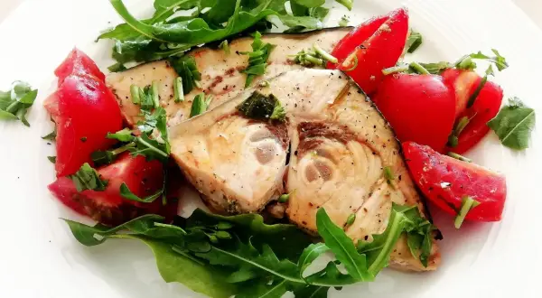 Spiedini di pesce spada in padella con pomodorini freschi e rucola, un piatto leggero e saporito.