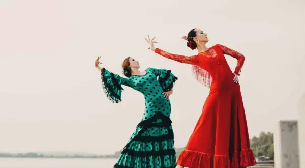 Dos mujeres bailan flamenco. Una con vestido verde de lunares, la otra con rojo. Inspiración para palos del flamenco para niños.