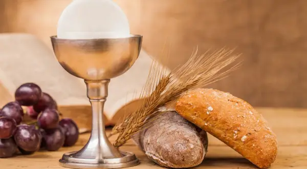 Kielich z hostią, winogrona, chleb i kłosy zbóż – symbole Eucharystii na drewnianym stole.