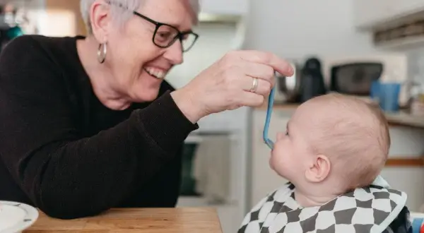 Glad mormor matar bebis med smakportioner. Första maten för en 4 månader gammal bebis.