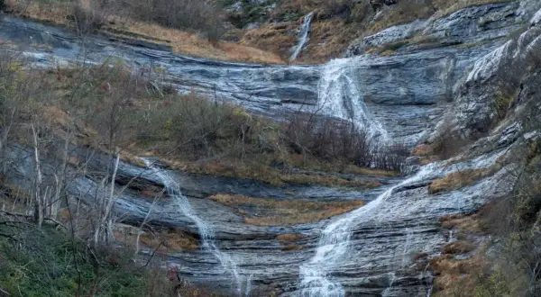 Le cascate della Volpara scendono su rocce stratificate, con vegetazione autunnale e alberi spogli che incorniciano il paesaggio.