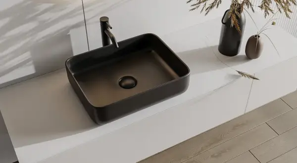 Nowoczesna, ciemna umywalka nablatowa 30x50 z baterią, na białym blacie, obok wazonów z trawą.