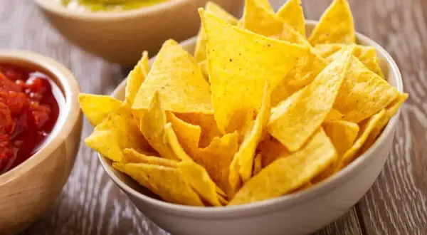 Nachos amarillos en un tazón, con salsa y guacamole al fondo.