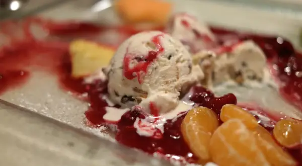 Cremiges Mascarpone Eis mit roter Fruchtsauce und Mandarinenstücken auf einem Teller.