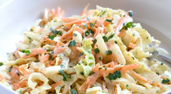 Chinakohl-Salat mit Karottenstreifen und Petersilie in einer weißen Schüssel.