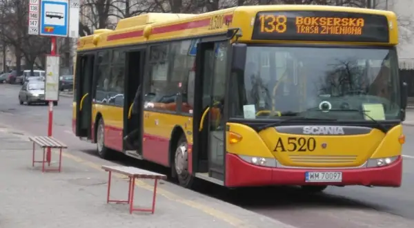 Żółto-czerwony autobus 138 warszawa z otwartymi drzwiami na przystanku.