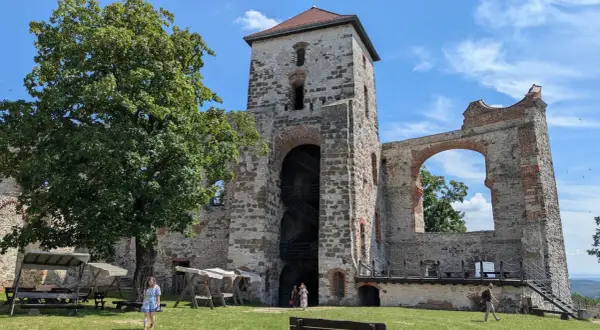 Ruiny zamku Tenczynek z wieżą i łukiem, na tle błękitnego nieba z chmurami.
