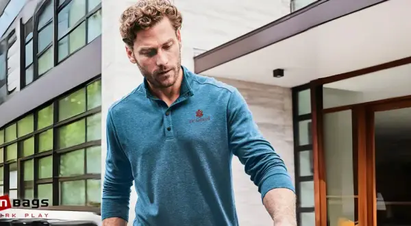 Mann trägt ein blaues Henley Shirt mit Knopfleiste und rotem Logo. Was ist ein Henley Shirt? Ein lässiges Oberteil mit Kragen und Knopfleiste.