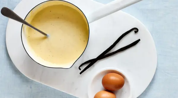 Zutaten für vanillesauce selber machen: ein Topf mit cremiger Sauce, zwei Eier und zwei Vanilleschoten.