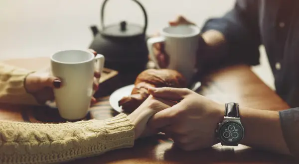 Dłonie trzymające kubki z kawą i croissant, symbolizujące czułe komplementy dla kobiety.