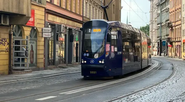Niebieski tramwaj z napisem "Biskupin" na wyświetlaczu, jadący po brukowanej ulicy w mieście.
