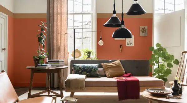 Wohnzimmer mit orangefarbenen Wänden, die mit abriebfester Farbe gestrichen sind. Ein Sofa, ein Tisch mit Büchern und Pflanzen.