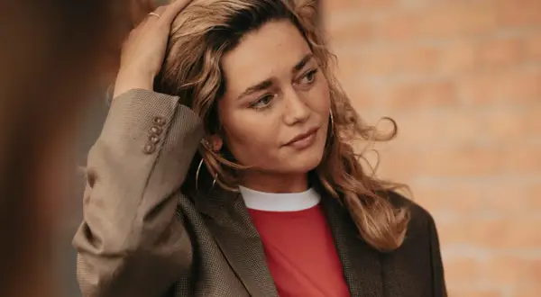 Kobieta z blond włosami w marynarce i czerwonej koszulce, dotykająca włosów.