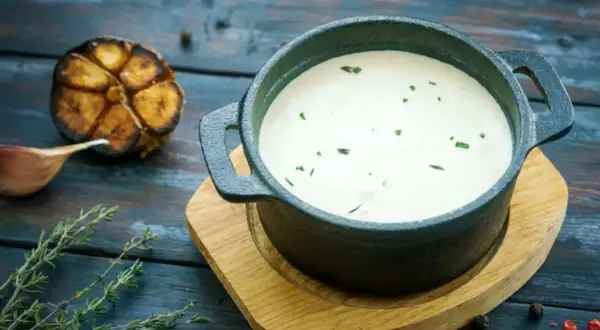 Cremoso alioli con leche, servido en cazuela de hierro fundido, acompañado de ajo asado y tomillo fresco.