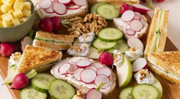 Un plateau d'apéro dinatoire plancha : toasts au fromage frais et radis, mini sandwichs concombre, dés de fromage, noix et quartiers de pomme.