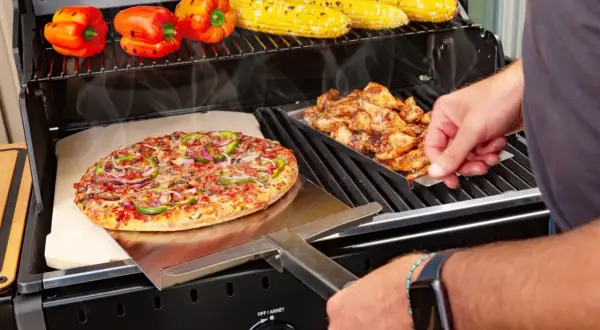 Na ruszcie grilla piecze się pyszna pizza z grilla, obok kurczak i kukurydza.