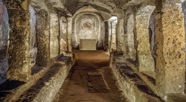 Corridoio sotterraneo con sedute in pietra e affreschi sbiaditi, parte dell'antico borgo di Sutri.