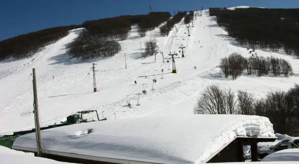 Piste innevate e skilift attivi sul monte Piselli, stazione sciistica con alberi spogli e cielo azzurro.