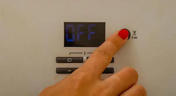 Dito che preme il pulsante per il reset caldaia Immergas. Lo schermo mostra "OFF".