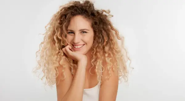 Uśmiechnięta kobieta z burzą blond loków, które tworzą piękne **skręty włosów**.