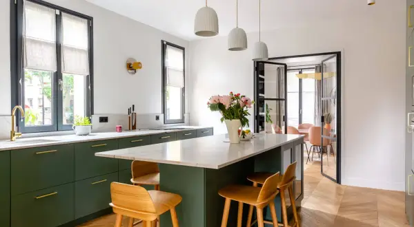 Cuisine moderne avec îlot central, tabourets en bois et armoires vert forêt. Une belle deco cuisine pour un intérieur lumineux.